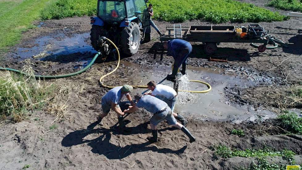 Terwijl één man van boven het water in het binnenste van de buis spuit, draaien de anderen de nieuw geplaatste pijp met behulp van metalen stang de grond in. Bas: „Bovenop de nieuwe buis zit een houten klos en daaraan is de stang bevestigd.” Daarna is het