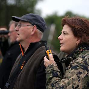 Erika Elsjan van WBE instrueert met een portofoon de loper in het perceel over de plek waar een warmteplek is gesignaleerd. De loper probeert zoveel mogelijk langs de kant van het perceel te gaan om het lange gras te sparen. Soms gebeurt het dat er een ha