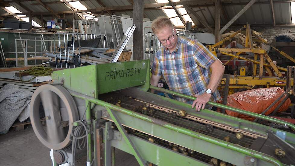 In de open schuur staat een kleine sorteermachine die handmatig werkt. Zodra Bakker aan het grote wiel draait, begint de machine te schudden en worden de aardappelen in drie maten gesorteerd.