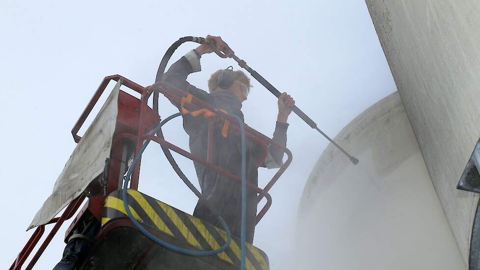 Erwin Folmer, medewerker van het schoonmaakbedrijf en tevens zoon van de kalverhouder, spuit de silo’s van beneden naar boven af. Dit voorkomt dat het vuile water in streepjes over het oppervlakte loopt en zo ongelijkmatig inbrand.