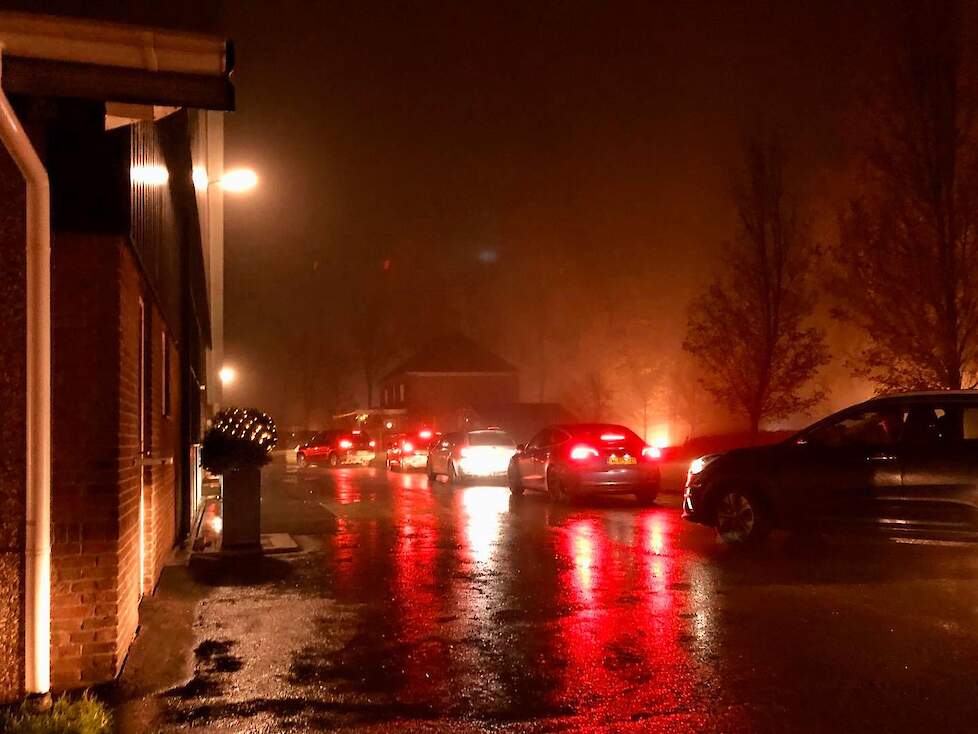 Filerijden langs verlichte boerderijen in Flevoland.